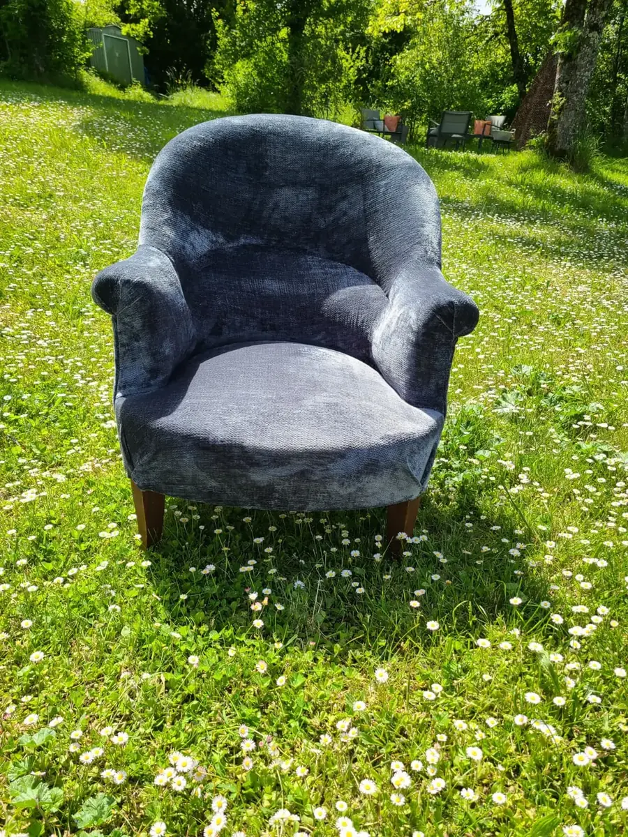 Fauteuil crapaud en velours bleu-gris, installé en extérieur dans un pré fleuri