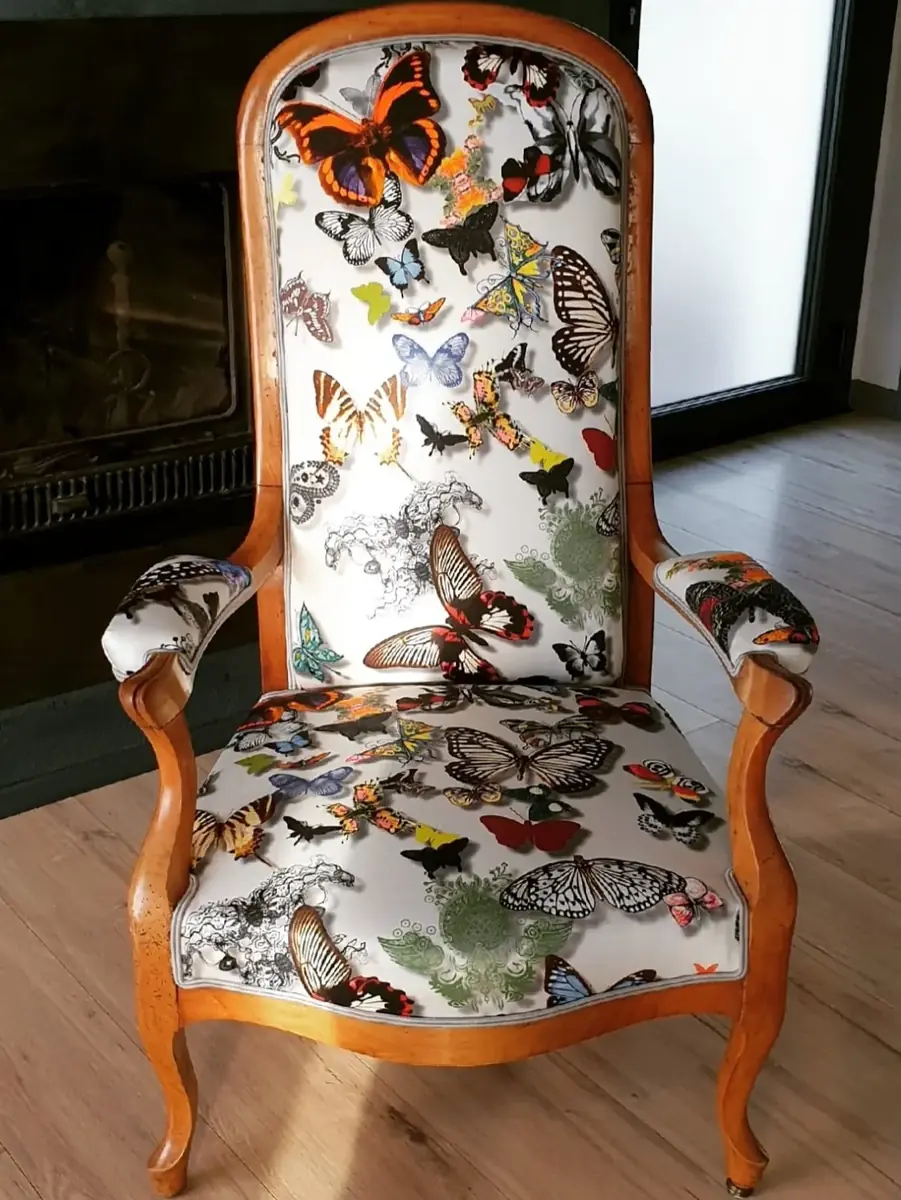 Fauteuil voltaire à tissu blanc imprimé de papillons multicolores, devant une cheminée